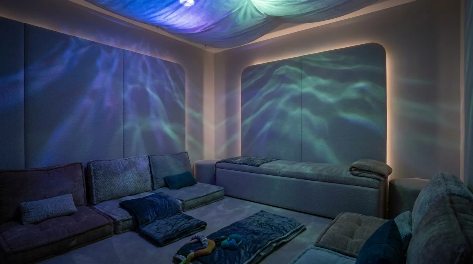 A near-dark sensory room with slow drifting light and floor cushions