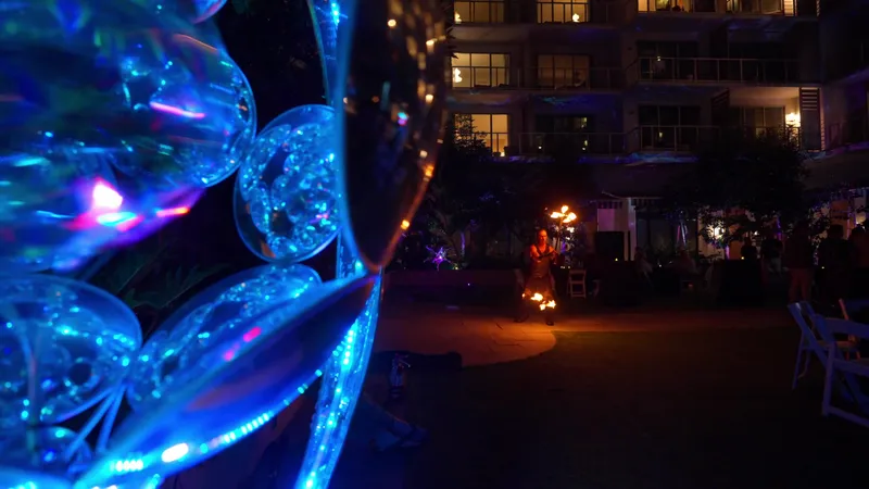 A fire performer at Mission Pacific Hotel, seen through a mirrored art installation with the lit building behind